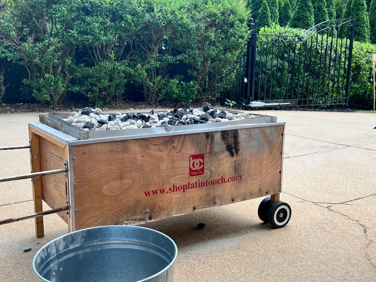 Wooden roasting box in a driveway with charcoal spread across its top tray