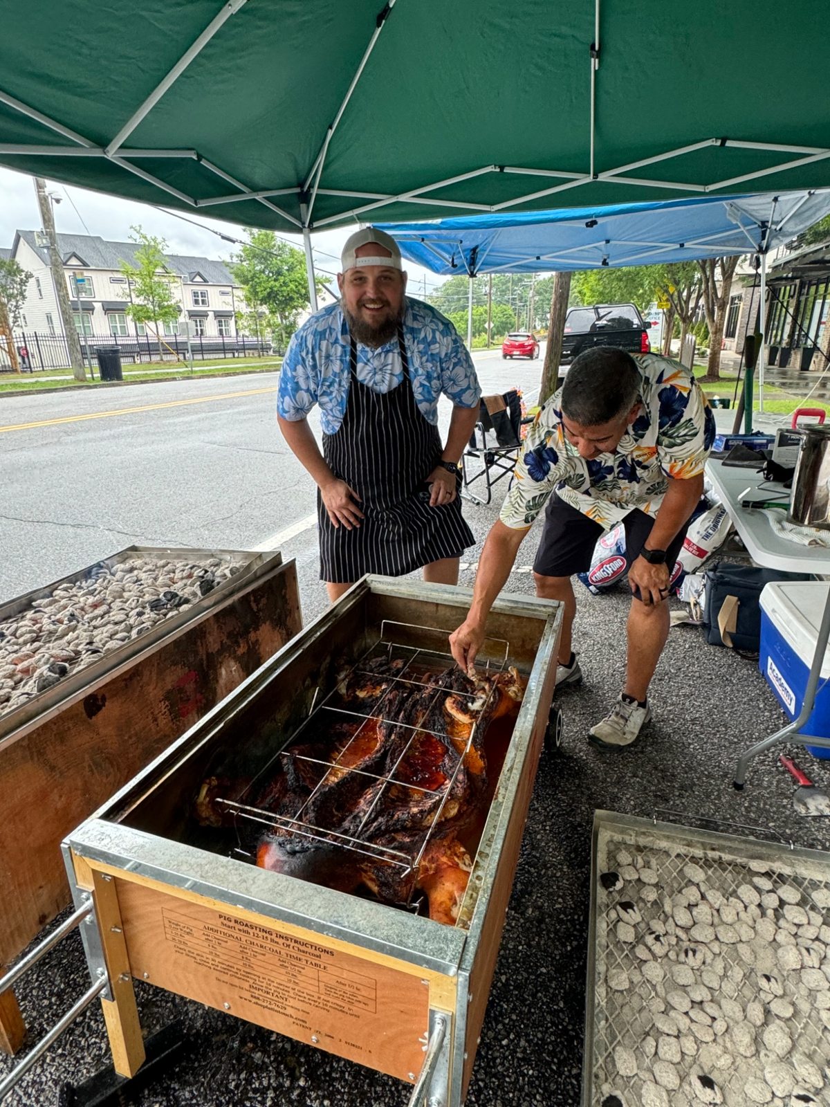Dan checking a roasting hog while another cook stands beside the box