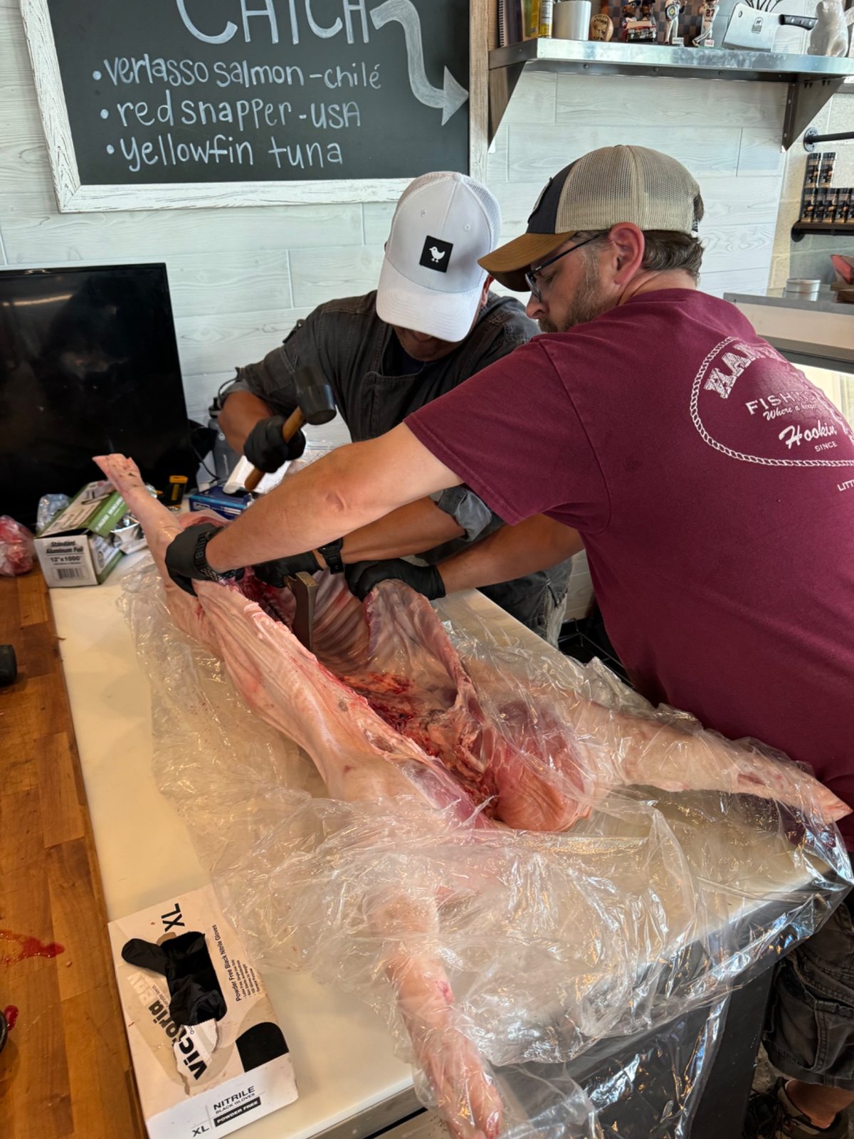 Two people working together to butterfly a hog on the butcher shop counter