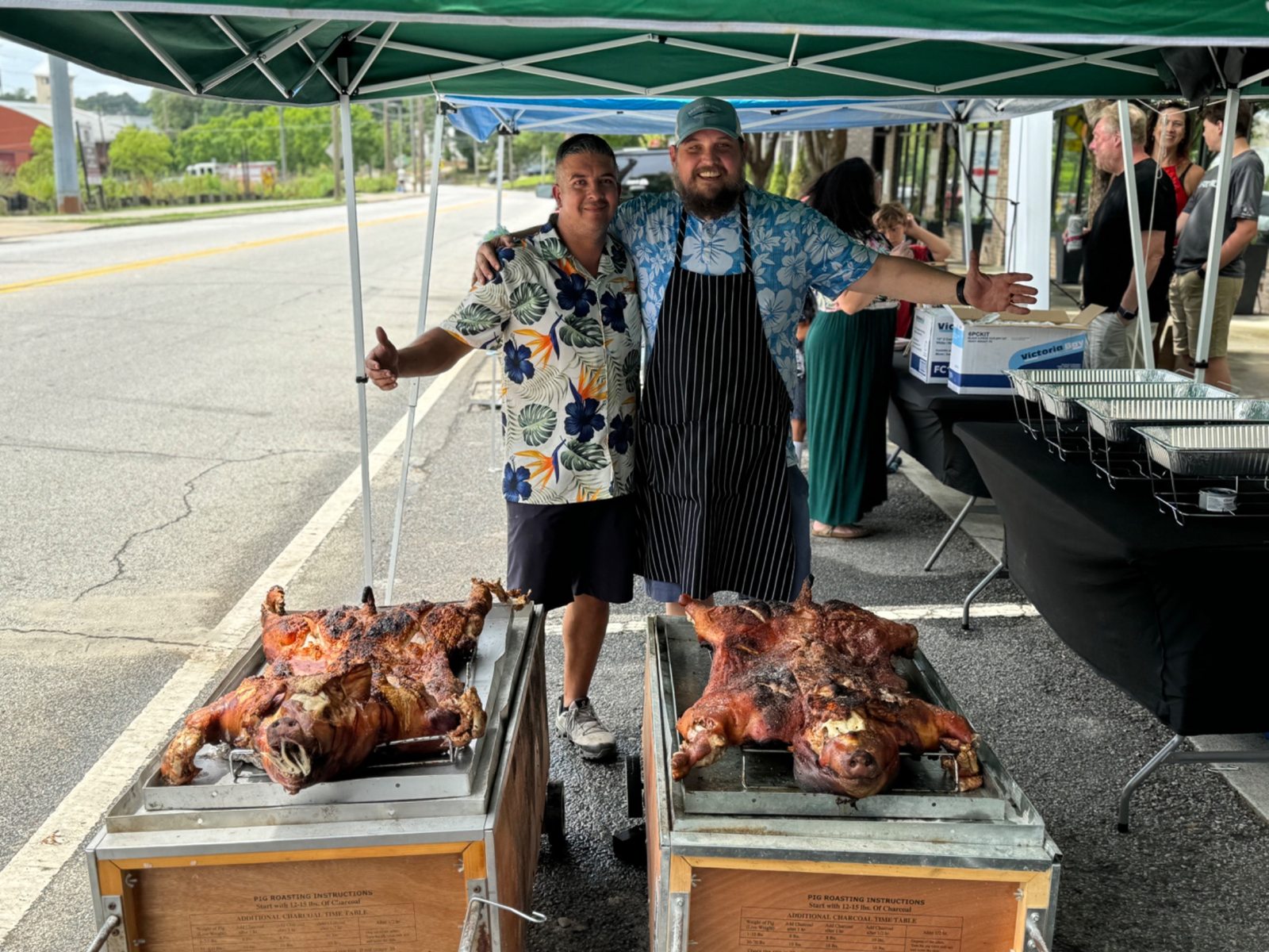 Two cooks standing behind two finished roasted hogs outside Frazie’s